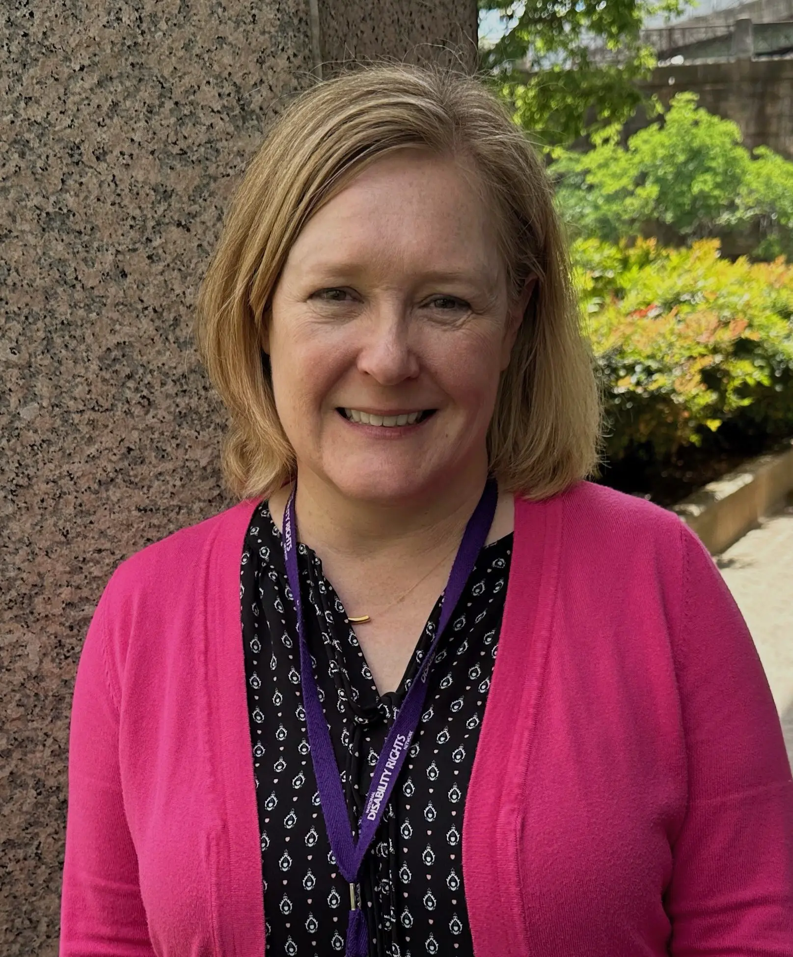 Portrait of Megan, a white woman with blonde hair. She is wearing a pink cardigan
