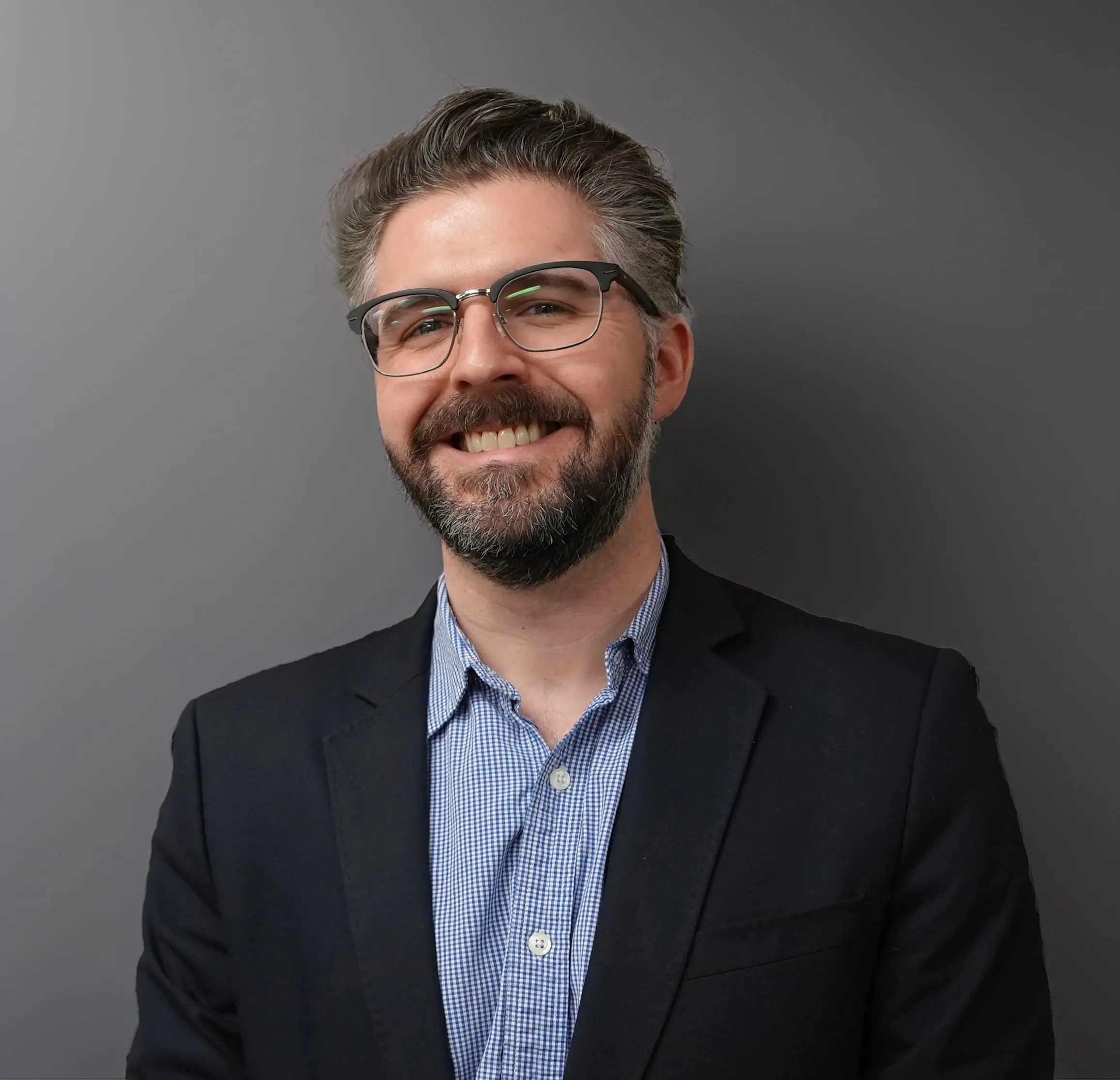 Andrew is a white male in his late 30s with dark and gray hair and short beard. He is wearing a blue blazer and blue shirt