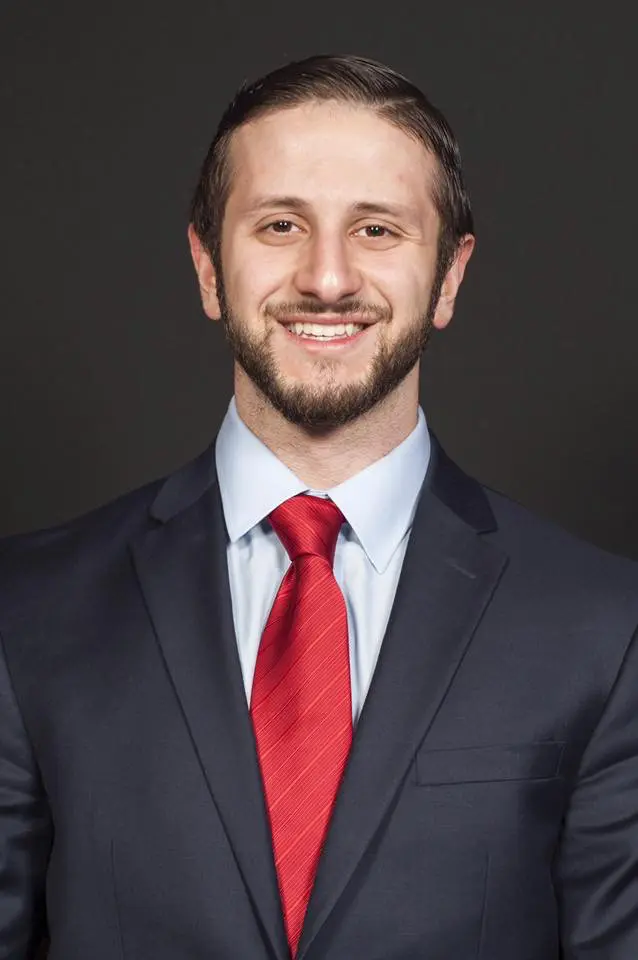 Photo of Mohammad Sarmini wearing a black suit and red tie as he smiles at the camera.