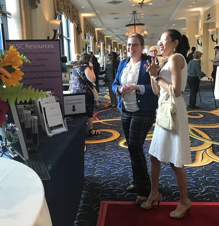 Two conference attendees stand in front of an exhibit table