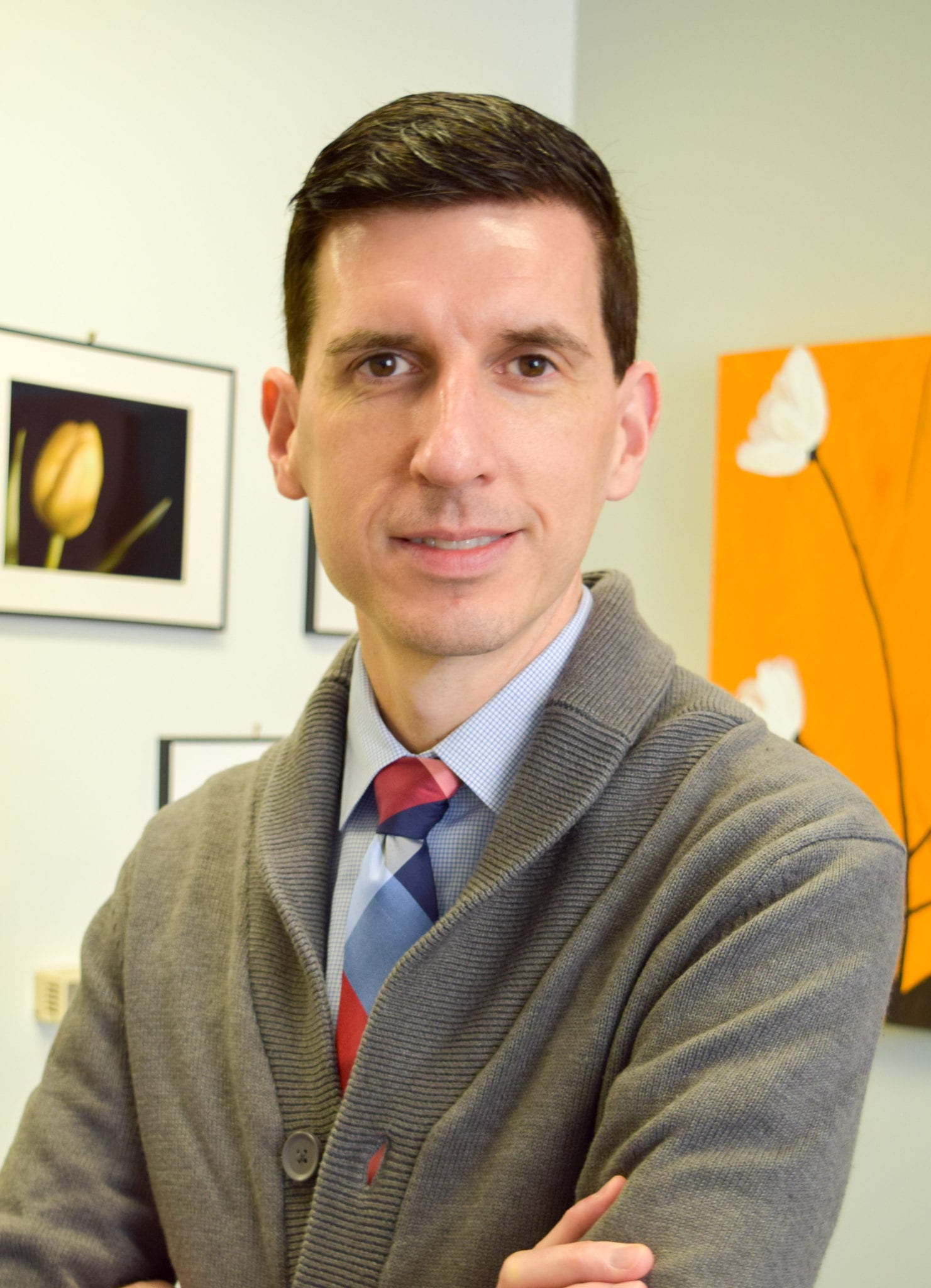 Portrait of David Card, a white man with dark hair wearing a grey sweater and colorful tie.