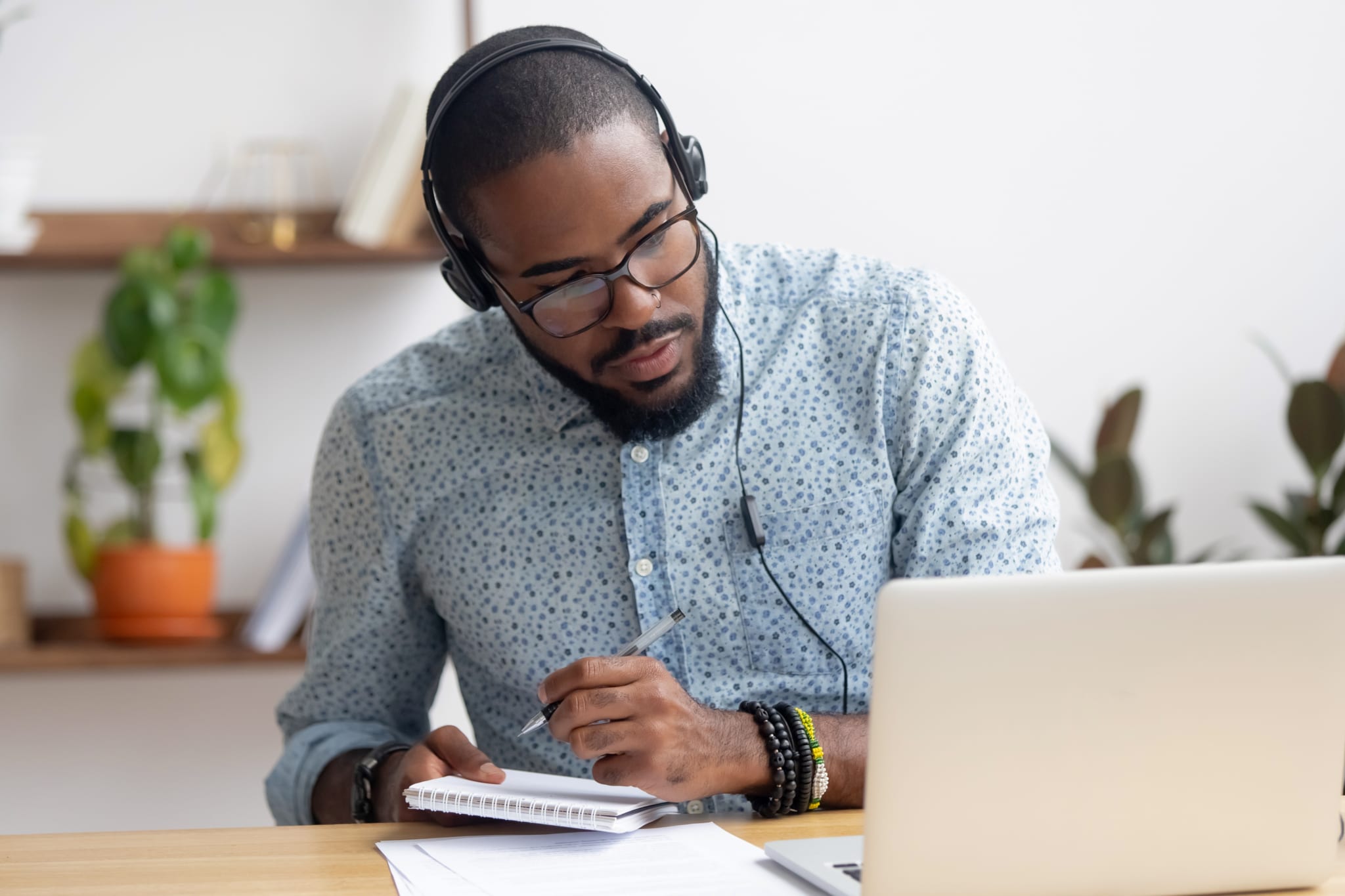 Focused businessman in headphones writing notes watching webinar