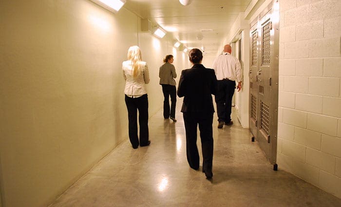 Three P&A staff and an administrator of a prison in Washington state walk down a hall with cells to the right