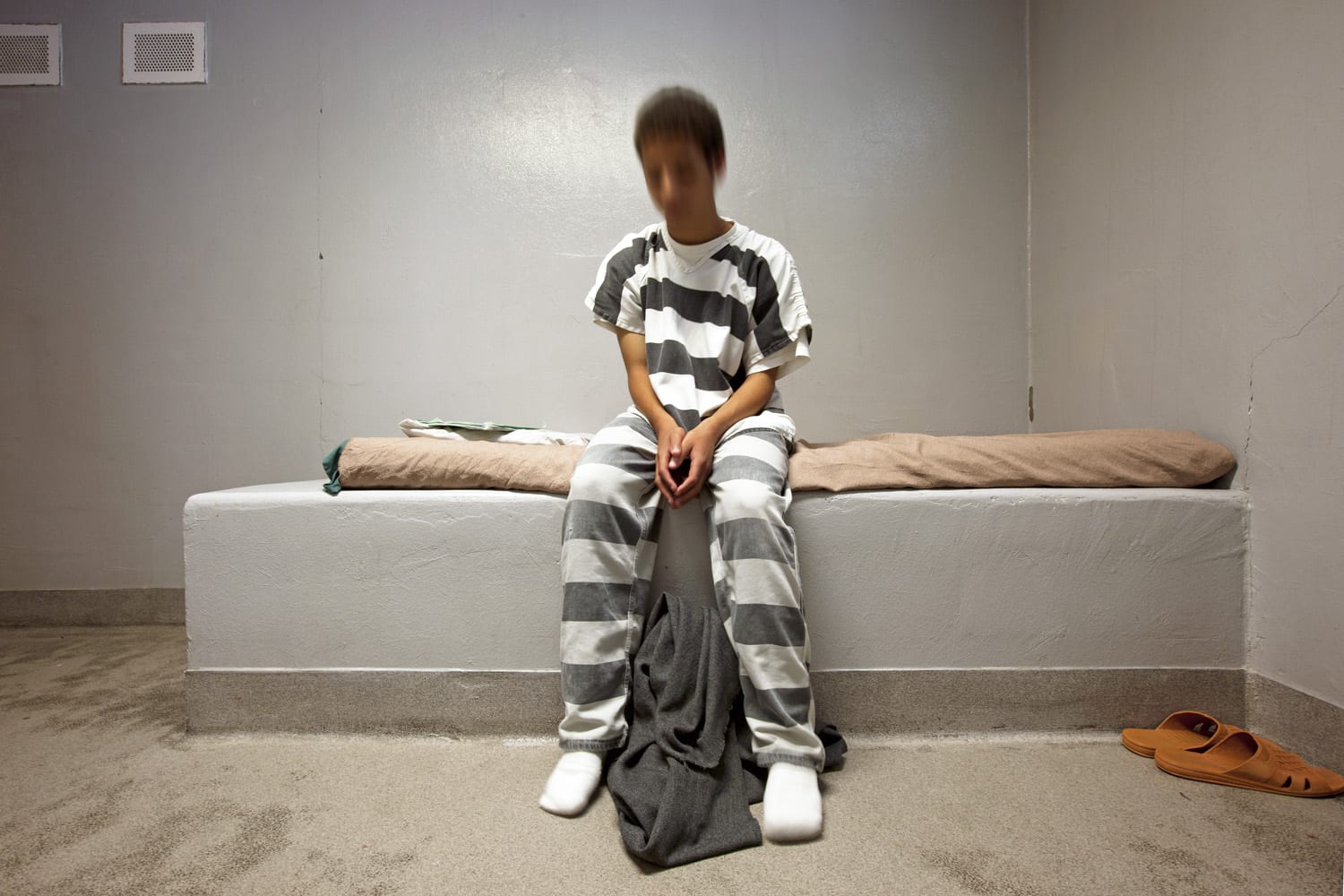 Child in striped jumpsuit sits in an isolation cell. Photo by Richard Ross.