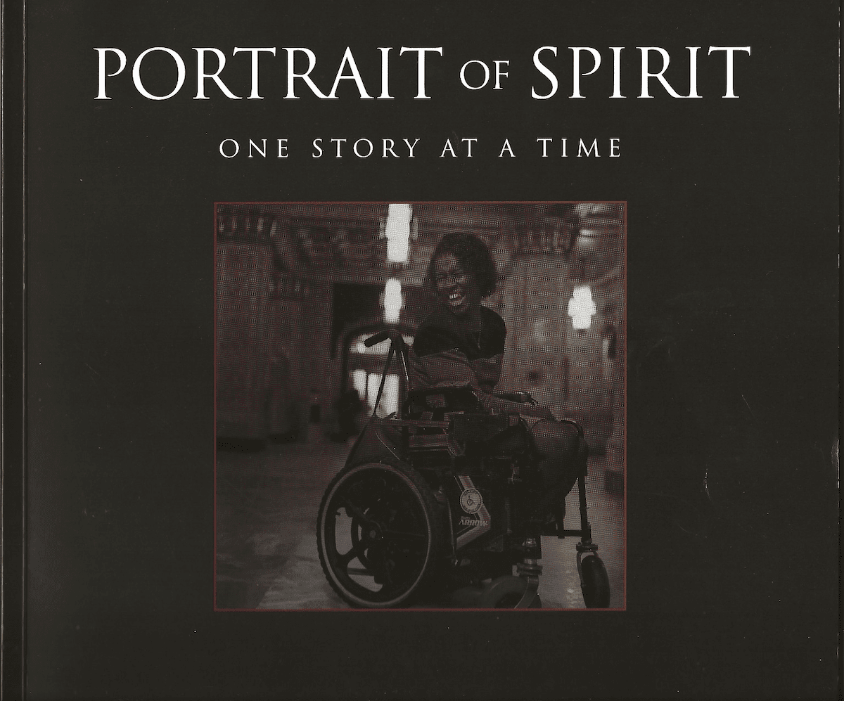 A book with the title "Portrait of Spirit: One Story at a Time" with a photo of Kate Gainer smiling in her wheelchair in a large marble detailedroom