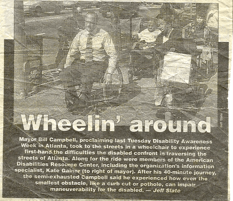 Newspaper clipping with the title “Wheelin’ around,” Mayor Bill Campbel, proclaiming last Tuesday Disability Awareness Week in Atlanta, took to the streets in a wheelchair to experience first-hand the difficulties the disabled confront in traversing the streets of Atlanta. Along for the ride were members of the American Disabilities Resource Center, including the organization’s information specialist, Kate Gainer (to the right of mayor). After his 40-minute journey, the semi-exhausted Campbell said he experienced how even the smallest obstacle, like a curbcut of a pothole, can impair maneuverability to the disabled – Jeff Slate… end clipping
