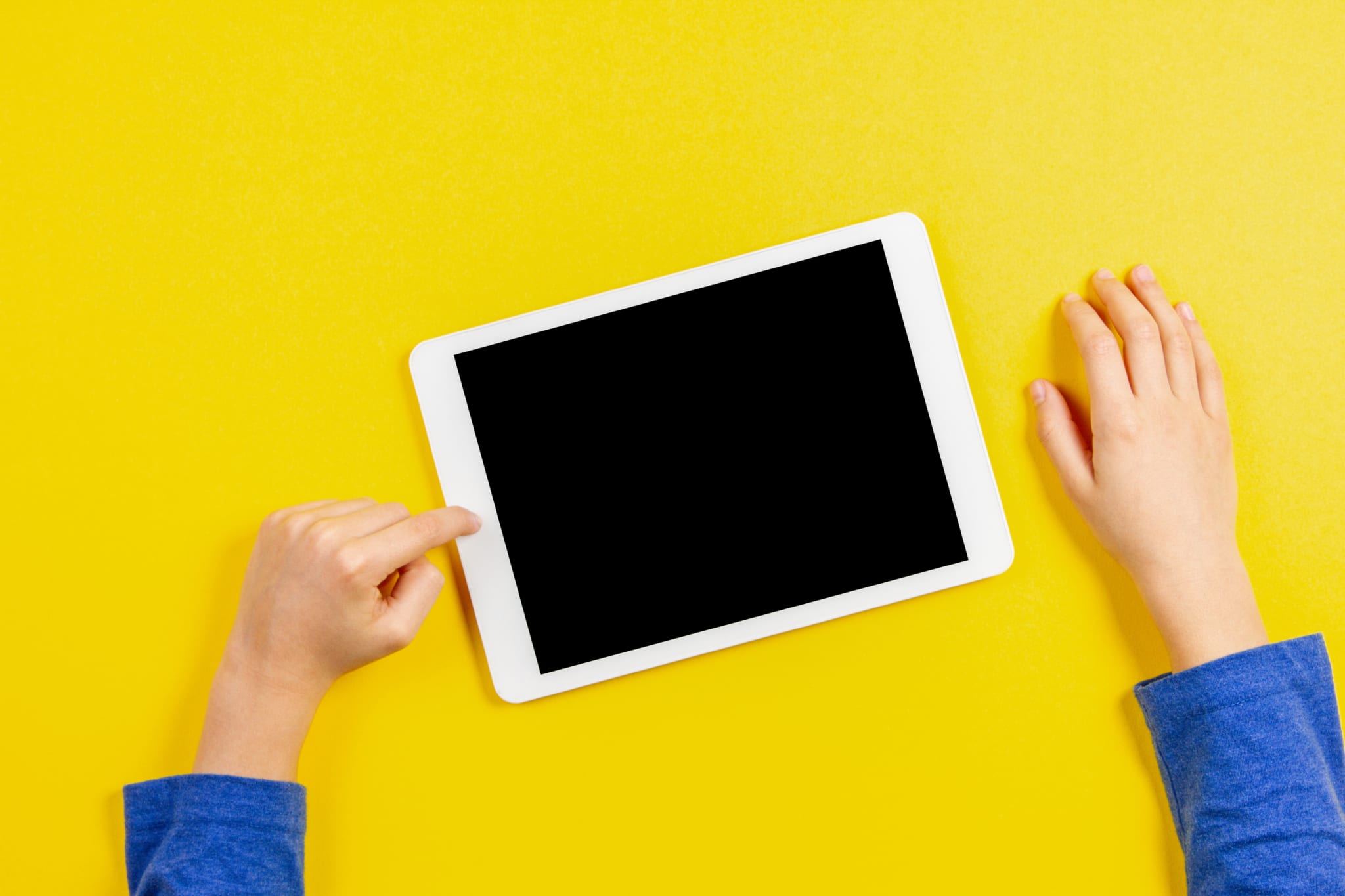 Kid hands with tablet computer on yellow background stock photo
