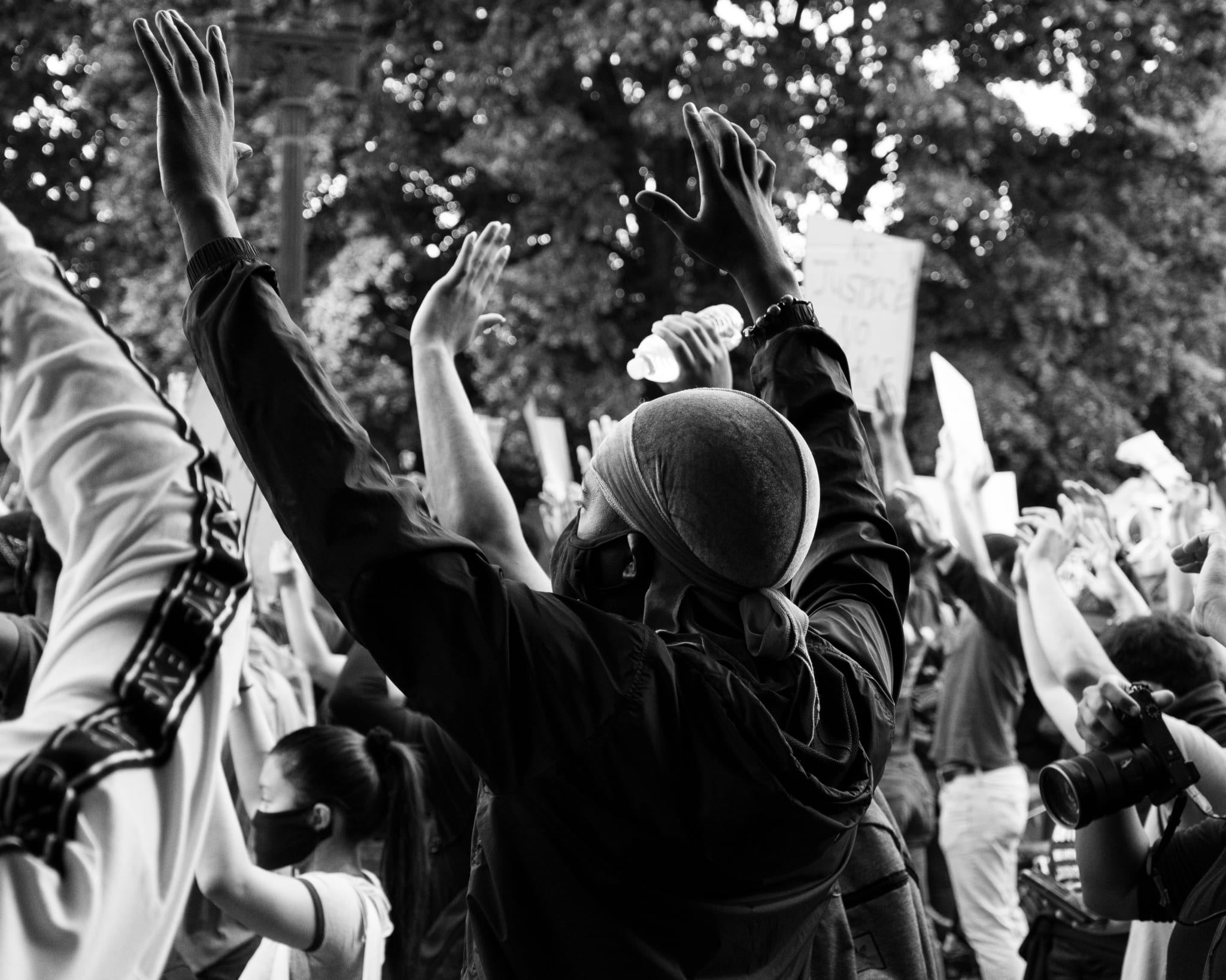 Black Lives Matter Protest in DC, a black male wearing a mask holds his hands up among others in a crowd. (Instagram: @koshuphotography)