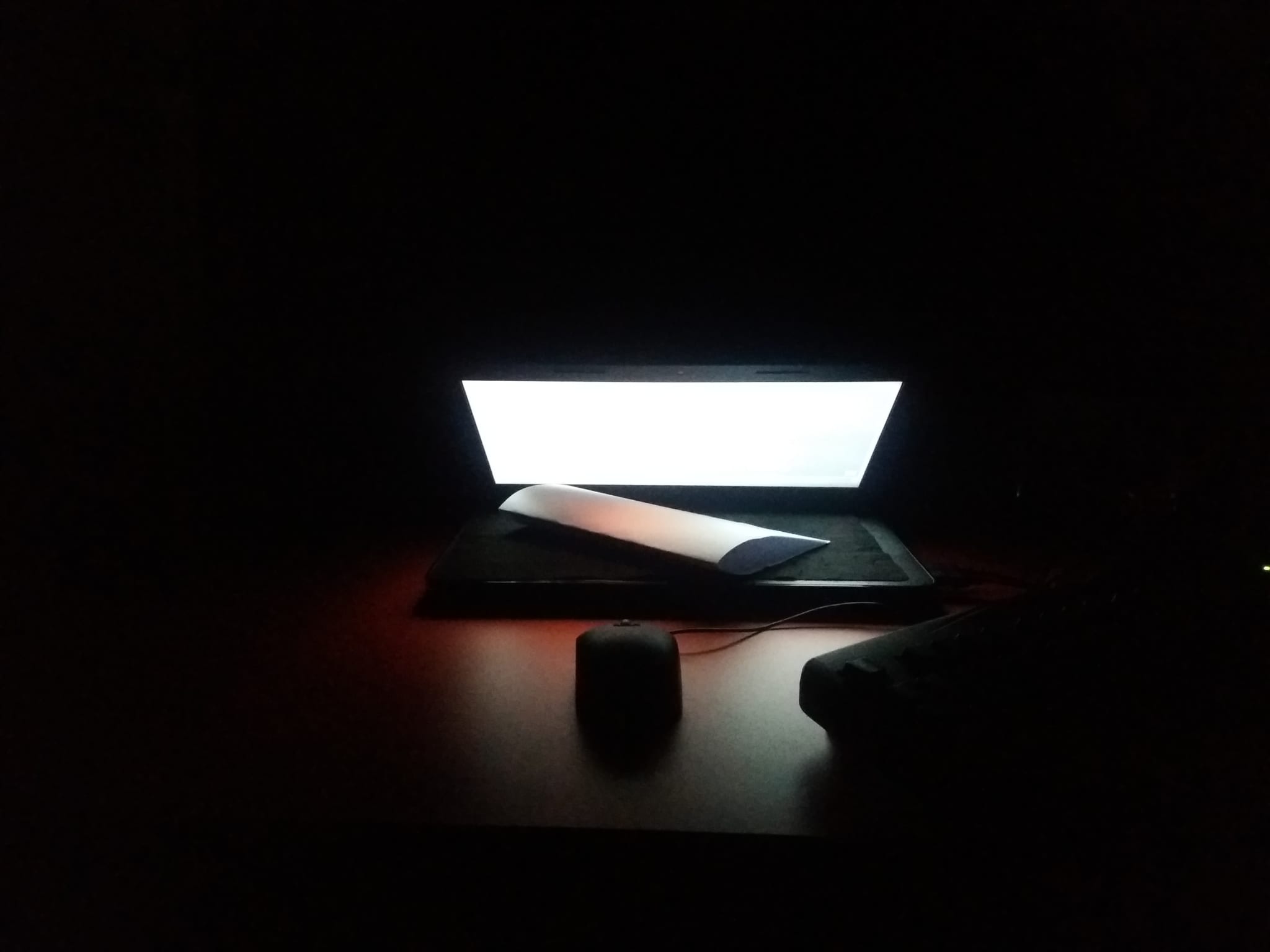 laptop in dark at night on table with mouse, lamp, paper.