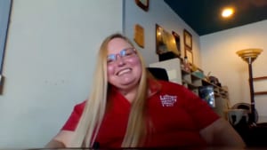 Teresa, a woman with blonde hair wears a red SABE shirt and smiles for the camera