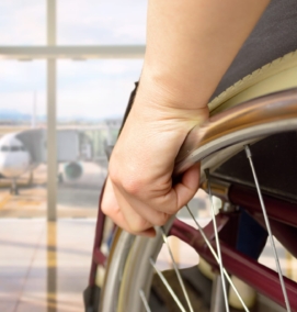 Close up of a hand on a wheel of a manual wheelchair. In the background is an airplane on a tarmac.
