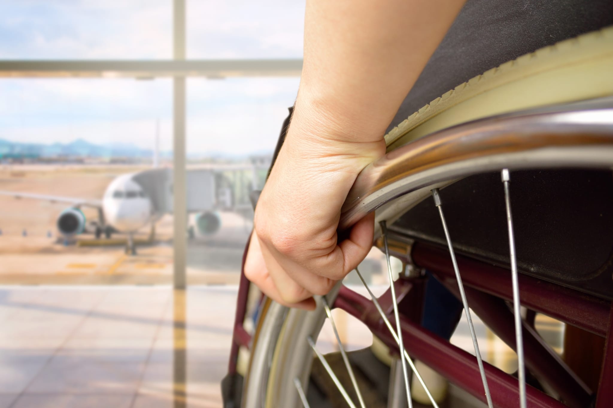 Close up of a hand on a wheel of a manual wheelchair. In the background is an airplane on a tarmac.