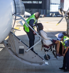 Woman in airplane aisle chair being carried onboard