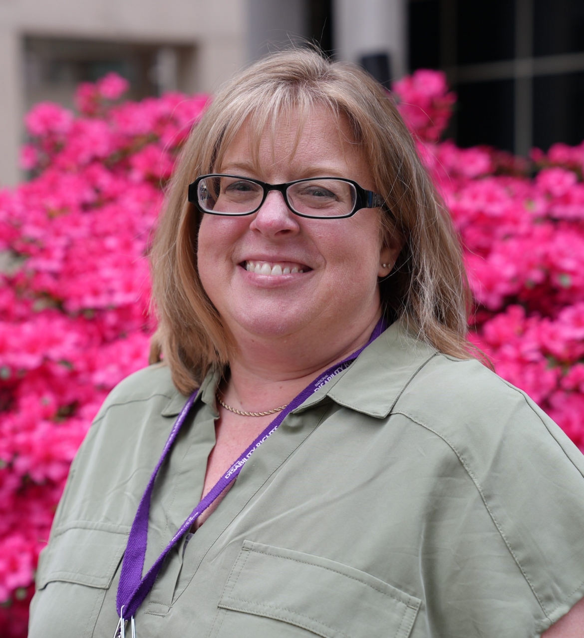 Picture of Stacie Browning. She is a white woman with blonde hair and glasses. She is smiling in front of pink flowers.