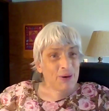 Mary-Ann, an older woman with white hair, wears a pink top and looks to the camera