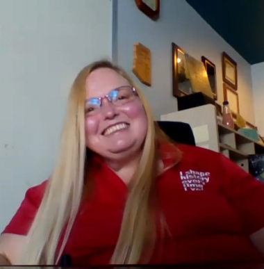 Teresa, a woman with blonde hair wears a red SABE shirt and smiles for the camera